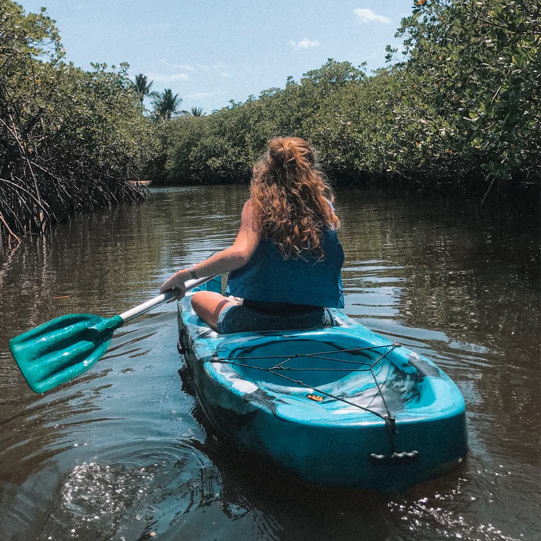 Caiaque descendo o rio em Trancoso, água espelhada, mangues e coqueiros nas margens