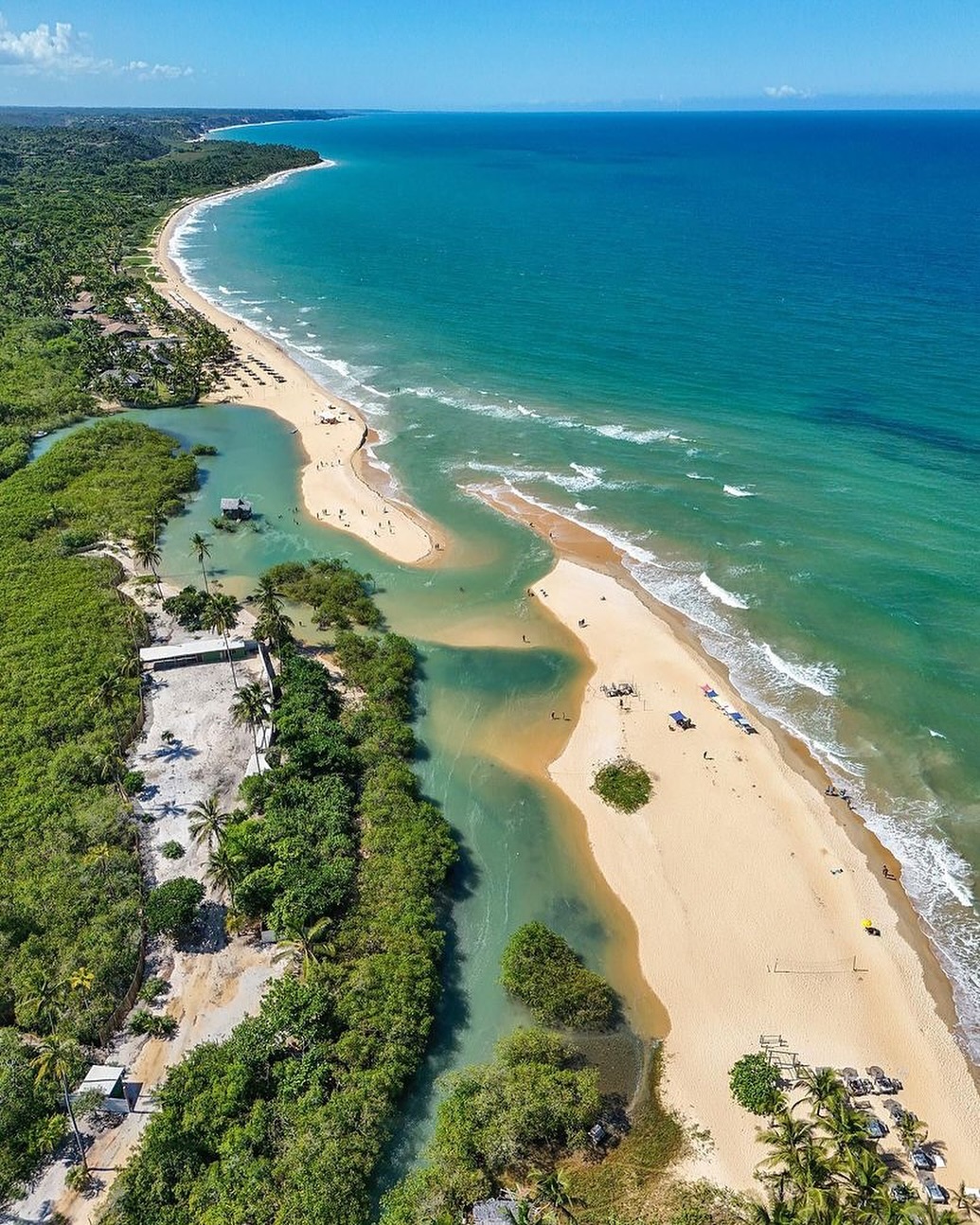 Vista aérea da praia do Rio da Barra em Trancoso — areia clara, mar verde-turquesa, mata atlântica e o rio desaguando no oceano