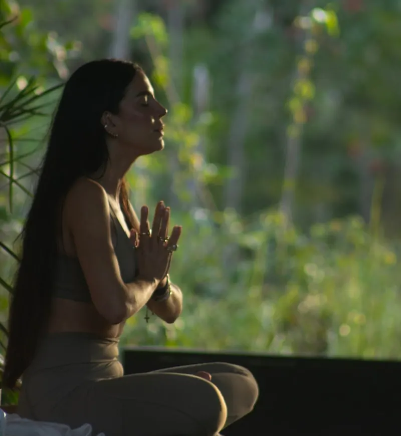Carmem Savazzi meditando de olhos fechados em meio à mata