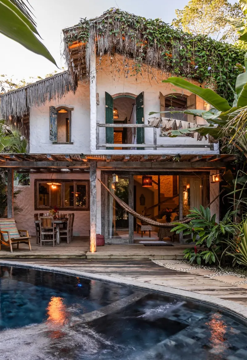 Casa de dois andares com rede na varanda e piscina iluminada ao entardecer