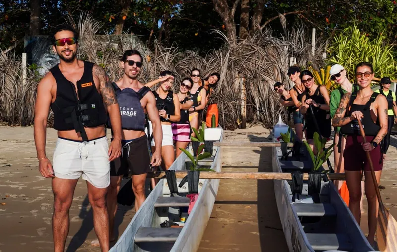 Participantes sorrindo de colete ao lado das canoas na praia