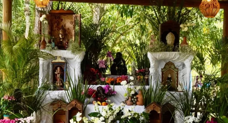 Altar com flores, velas e imagens montado no meio do verde